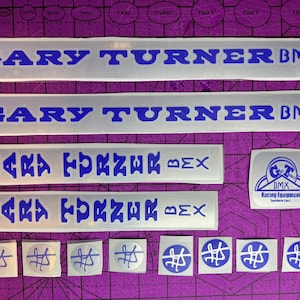 May include: A set of vintage bicycle decals in silver and blue. The decals feature the text "GARY TURNER BMX" in a bold, blocky font. There are also smaller decals with the text "GARY TURNER BMX" in a more stylized font. The decals are in excellent condition and would be a great addition to any vintage BMX bike.