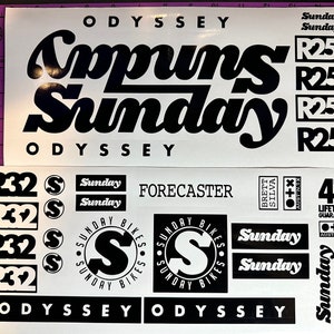 May include: A set of black and white bicycle stickers with the words "Copuns Sunday" and "Odyssey" printed on them. The stickers also include the words "Sunday Bikes" and "Forecaster".