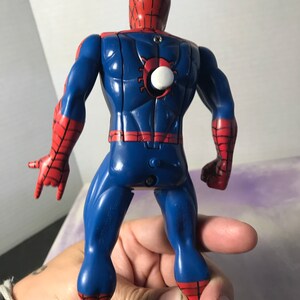 K&ouml;nnte beinhalten: Eine rote und blaue Plastik-Actionfigur von Spiderman. Die Figur hat einen Aufziehschl&uuml;ssel auf dem R&uuml;cken und ist mit ausgestreckten Armen posiert.