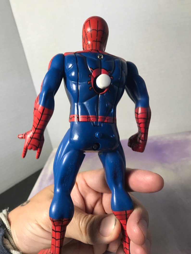 K&ouml;nnte beinhalten: Eine rote und blaue Plastik-Actionfigur von Spiderman. Die Figur hat einen Aufziehschl&uuml;ssel auf dem R&uuml;cken und ist mit ausgestreckten Armen posiert.