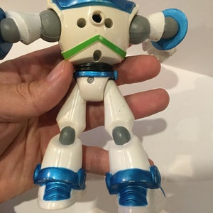 Pu&ograve; includere: Giocattolo robot bianco e blu con accenti grigi. Il robot ha un design verde sul petto ed &egrave; in posizione eretta con le braccia distese.