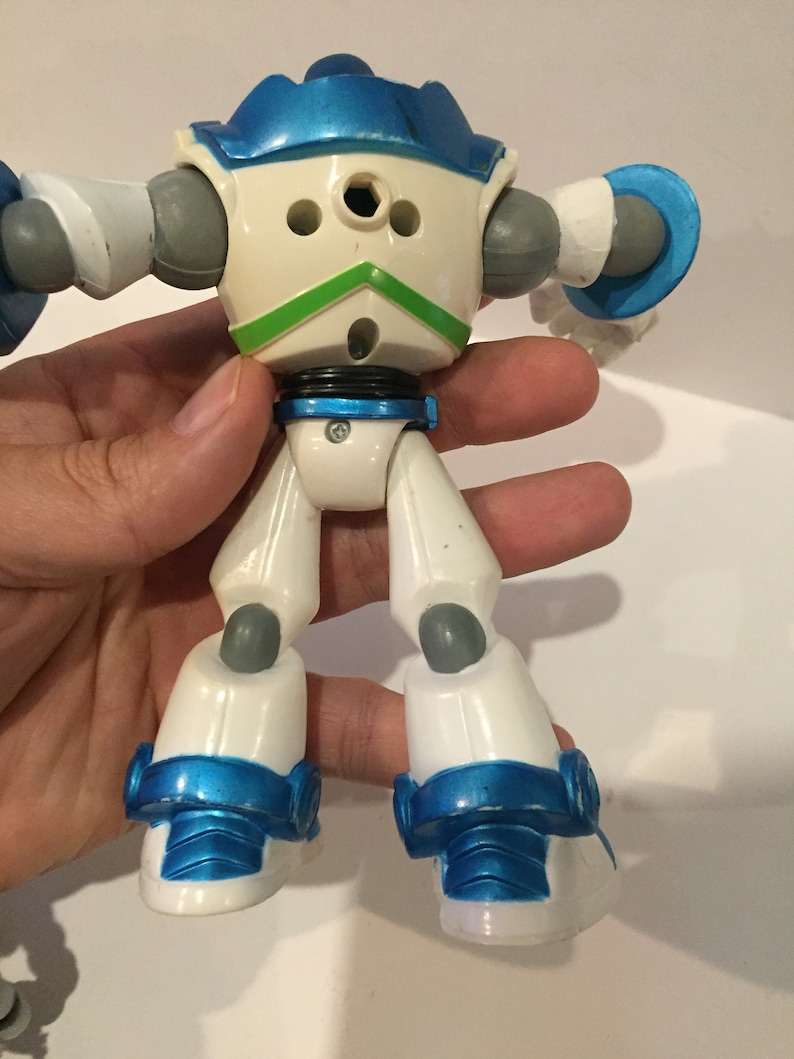 Pu&ograve; includere: Giocattolo robot bianco e blu con accenti grigi. Il robot ha un design verde sul petto ed &egrave; in posizione eretta con le braccia distese.