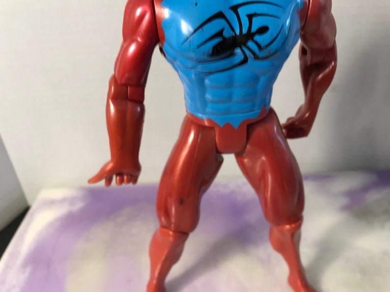 Puede incluir: Una figura de acci&oacute;n roja y azul con un dise&ntilde;o de ara&ntilde;a en el pecho. La figura tiene brazos y piernas articulados.