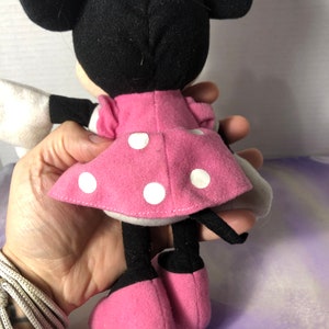 K&ouml;nnte beinhalten: Ein rosa-wei&szlig;es gepunktetes Kleid mit einer schwarzen Schleife auf dem Kopf. Das Pl&uuml;schtier hat schwarze Ohren und schwarze Schuhe.