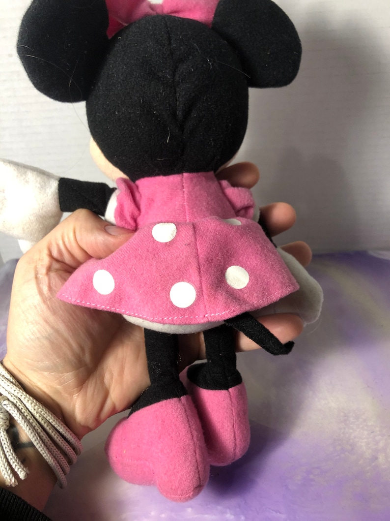 K&ouml;nnte beinhalten: Ein rosa-wei&szlig;es gepunktetes Kleid mit einer schwarzen Schleife auf dem Kopf. Das Pl&uuml;schtier hat schwarze Ohren und schwarze Schuhe.