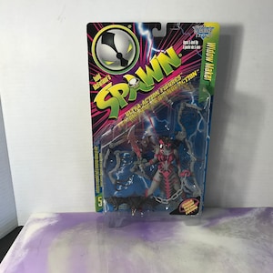May include: A plastic package containing a Widow Maker action figure from the Spawn series. The figure is pink and gray with a chain and a sword. The packaging is blue and black with the Spawn logo and the words "Ultra-Action Figures".
