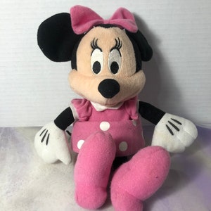 K&ouml;nnte beinhalten: Ein rosa und schwarzes Pl&uuml;schtier von Minnie Mouse mit einer rosa Schleife, wei&szlig;en Punkten auf ihrem Kleid und wei&szlig;en Handschuhen.