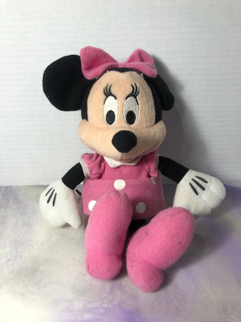 K&ouml;nnte beinhalten: Ein rosa und schwarzes Pl&uuml;schtier von Minnie Mouse mit einer rosa Schleife, wei&szlig;en Punkten auf ihrem Kleid und wei&szlig;en Handschuhen.