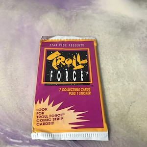 May include: A purple and yellow package of Troll Force trading cards. The package features a cartoon troll with the text "Troll Force" and "7 collectible cards plus 1 sticker".