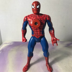 K&ouml;nnte beinhalten: Eine rote und blaue Actionfigur von Spider-Man mit einem roten Brustst&uuml;ck, das eine kreisf&ouml;rmige &Ouml;ffnung hat. Die Figur hat ein Netzdesign auf ihrem Anzug und ist mit ausgestreckten Armen posiert.