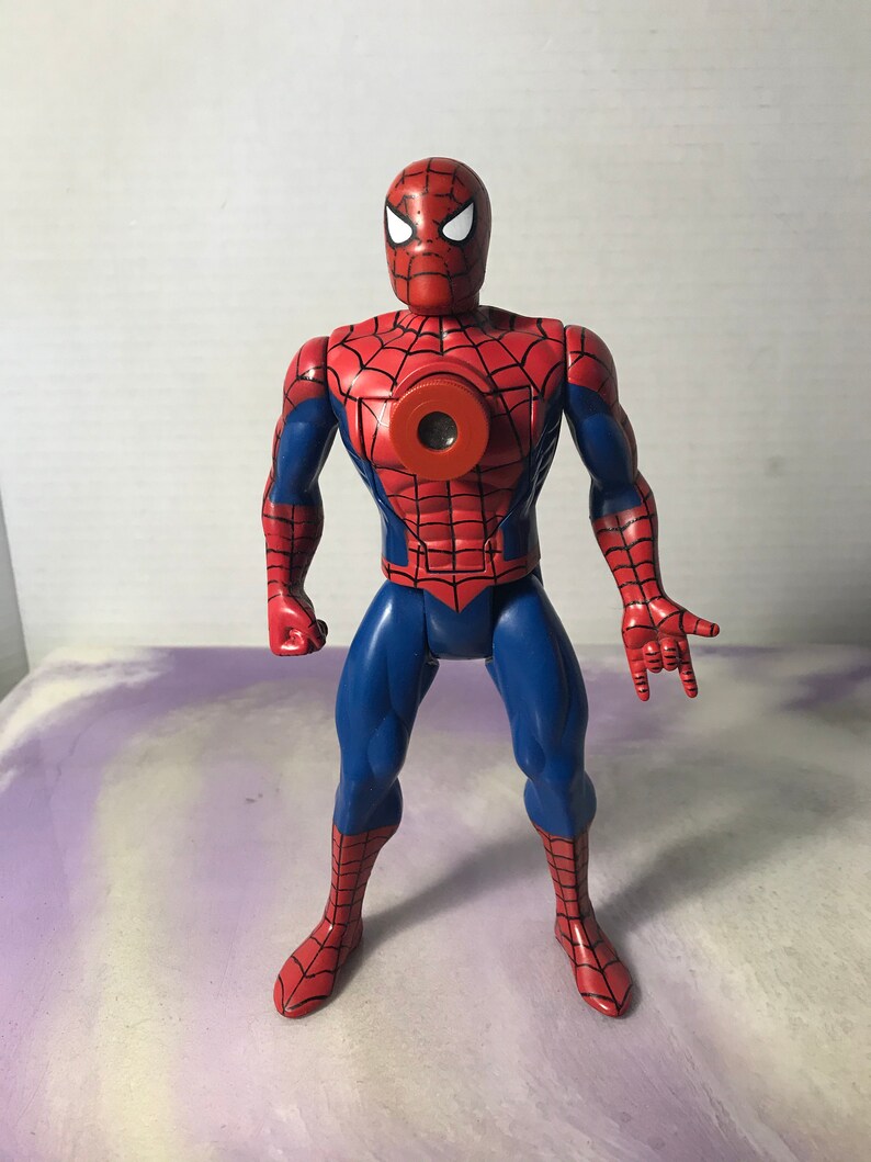 K&ouml;nnte beinhalten: Eine rote und blaue Actionfigur von Spider-Man mit einem roten Brustst&uuml;ck, das eine kreisf&ouml;rmige &Ouml;ffnung hat. Die Figur hat ein Netzdesign auf ihrem Anzug und ist mit ausgestreckten Armen posiert.