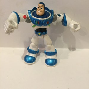 Pu&ograve; includere: Una action figure di plastica bianca e blu di Buzz Lightyear della serie Toy Story. La figura ha un casco blu e un corpo bianco con dettagli blu. La figura &egrave; in posa con le braccia distese.