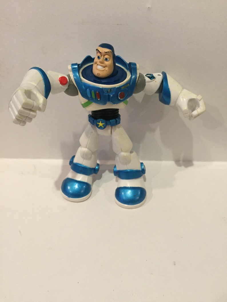Pu&ograve; includere: Una action figure di plastica bianca e blu di Buzz Lightyear della serie Toy Story. La figura ha un casco blu e un corpo bianco con dettagli blu. La figura &egrave; in posa con le braccia distese.
