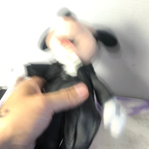 May include: A black and white plush toy with a black bow tie. The toy is being held by a hand.