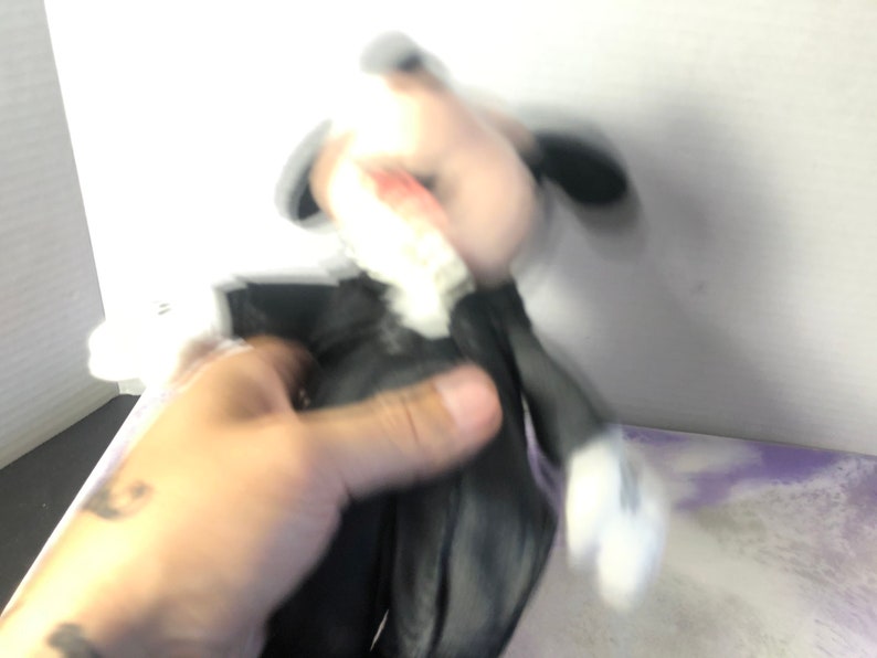 May include: A black and white plush toy with a black bow tie. The toy is being held by a hand.