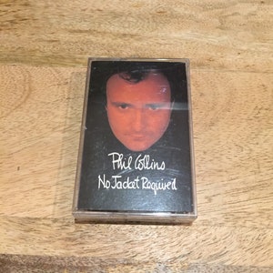 Peut inclure: Une cassette audio vintage de l'album "No Jacket Required" de Phil Collins. La pochette noire présente un portrait de Phil Collins et le titre de l'album en blanc. La cassette est dans un boîtier en plastique transparent.
