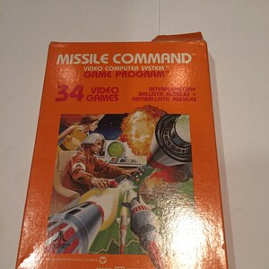 May include: Orange box with a picture of a person in a cockpit controlling missiles. The box is for a video game called "Missile Command" for the Atari Video Computer System. The box says "34 Video Games" and "Special Feature".