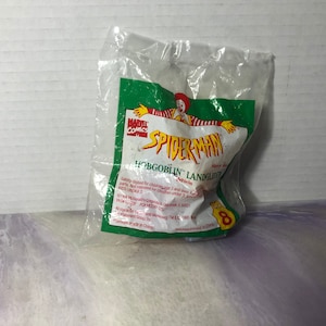 May include: A green and red plastic bag with a Spider-Man toy inside. The bag has the words "Marvel Comics" and "Spider-Man" on it. The toy is a green and red vehicle with the words "Hobgoblin Landglider Vehicle" on it.