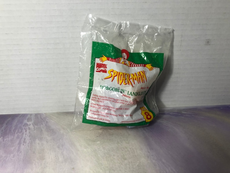 May include: A green and red plastic bag with a Spider-Man toy inside. The bag has the words "Marvel Comics" and "Spider-Man" on it. The toy is a green and red vehicle with the words "Hobgoblin Landglider Vehicle" on it.