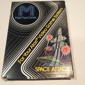 May include: A black box with a silver M Network logo and the text "For Your Atari* Video Game System" and "SPACE ATTACK VIDEO GAME CARTRIDGE". The box has a graphic of a spaceship shooting at a UFO.