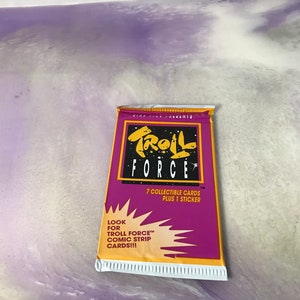 May include: A sealed pack of Troll Force comic strip cards. The packaging is primarily purple with a yellow and black logo. The text on the pack reads "7 Collectible Cards Plus 1 Sticker". The bottom of the pack reads "Look for Troll Force Comic Strip Cards!!!"