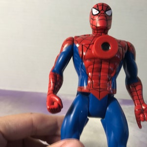 May include: A red and blue plastic action figure of Spider-Man. The figure has a web design on its chest and a black eye mask.