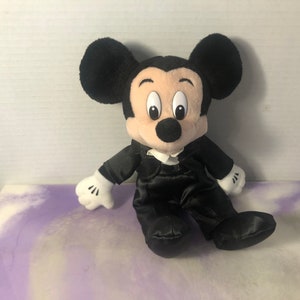May include: A black plush Mickey Mouse wearing a black tuxedo with a white bow tie.