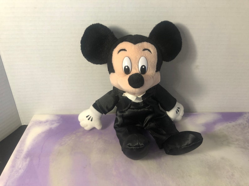 May include: A black plush Mickey Mouse wearing a black tuxedo with a white bow tie.