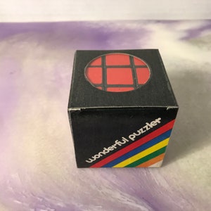May include: A black box with a red and black grid pattern on the top. The box has the words "wonderful puzzler" printed on the side in rainbow colors.