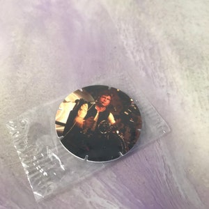 Può includere: Un oggetto da collezione circolare di Star Wars con un'immagine a colori di Han Solo in un abitacolo. L'immagine è racchiusa in una custodia di plastica trasparente. L'oggetto da collezione ha un bordo argentato ed è posto su uno sfondo viola chiaro.