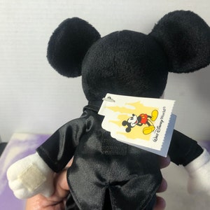 May include: Black plush Mickey Mouse wearing a tuxedo with a white tag that says "Walt Disney World".