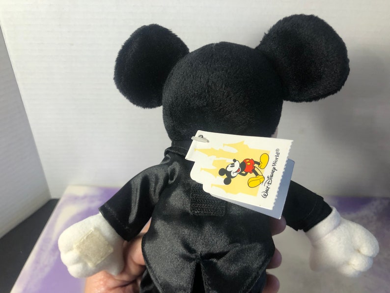 May include: Black plush Mickey Mouse wearing a tuxedo with a white tag that says "Walt Disney World".