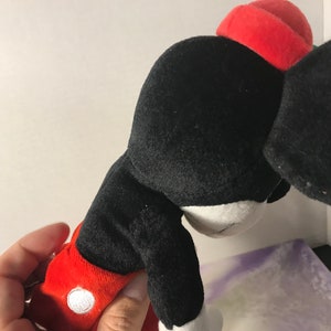May include: Black and red plush Mickey Mouse toy with a red hat. The toy is in a sitting position with its head tilted down.