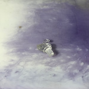 Peut inclure: Un bouchon de bouteille en verre transparent avec un motif de cygne. Le bouchon est posé sur une surface violette et blanche.