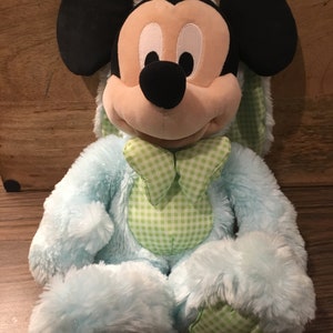 May include: A blue plush Easter bunny Mickey Mouse toy with green gingham accents. The toy has a fluffy texture and a friendly expression.