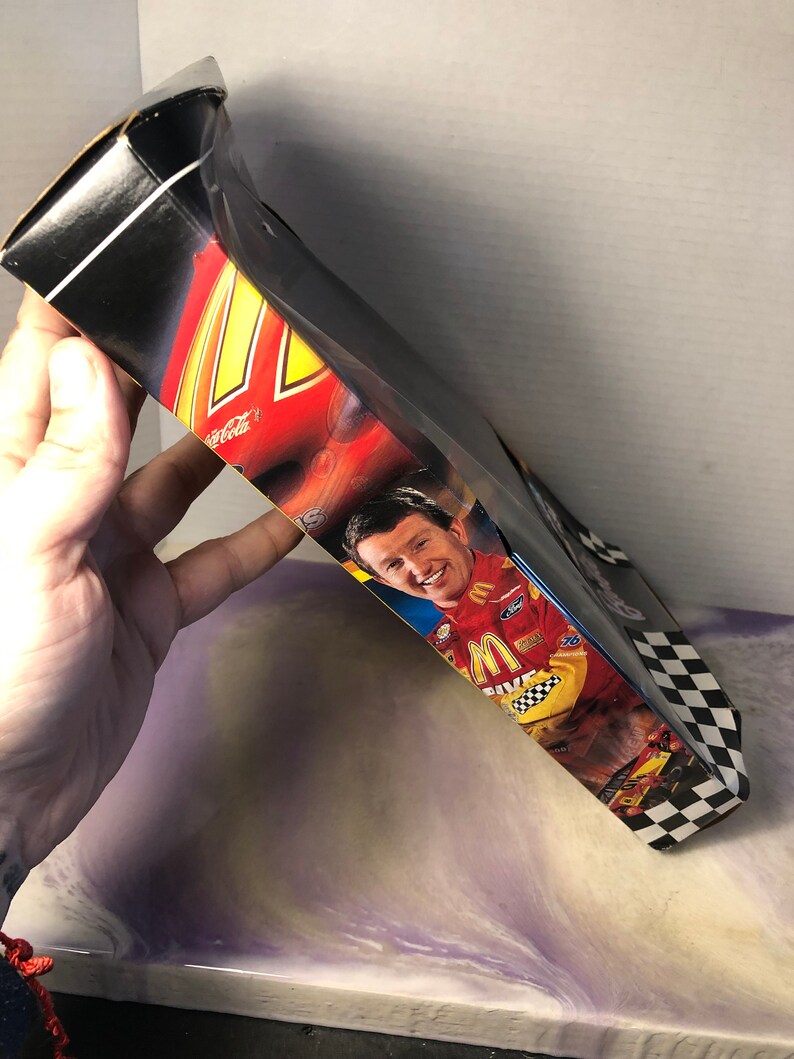 May include: A black and white checkered box with a red, yellow, and black race car on the front. The box features a picture of a race car driver wearing a yellow and black racing suit with the McDonald's logo. The box also has the words "Coca-Cola" and "M&M's" on it.