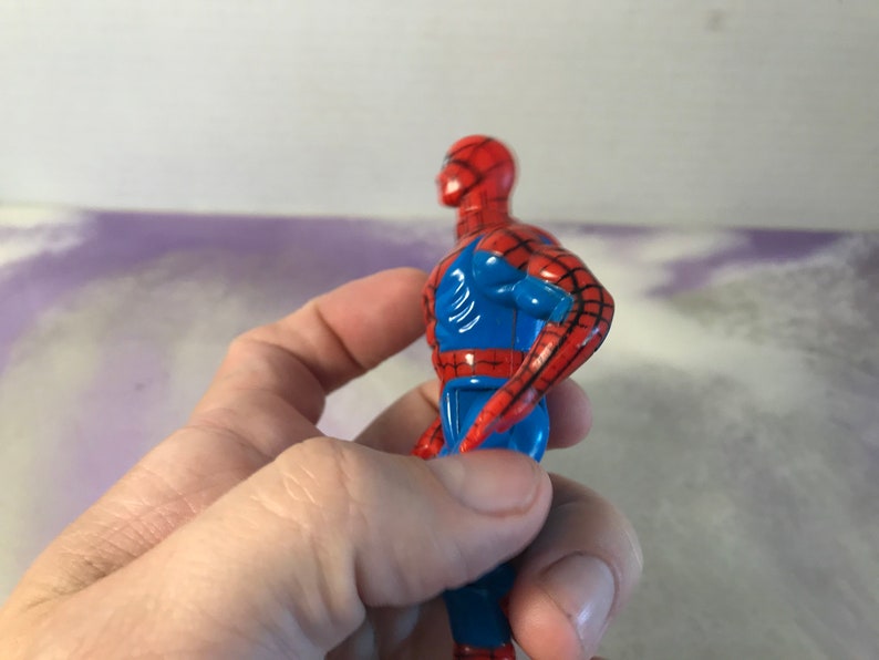 May include: A red and blue plastic action figure of Spider-Man. The figure is posed with its right arm raised and its left arm bent at the elbow.