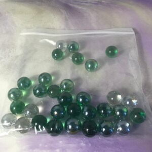 Peut inclure: Un sac en plastique rempli de billes de verre vertes et transparentes. Les billes sont de différentes nuances de vert et certaines sont irisées.