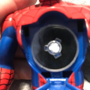 May include: A blue and red plastic action figure of Spiderman with a clear plastic disc on the back. The disc has a silver gear-like design in the center.