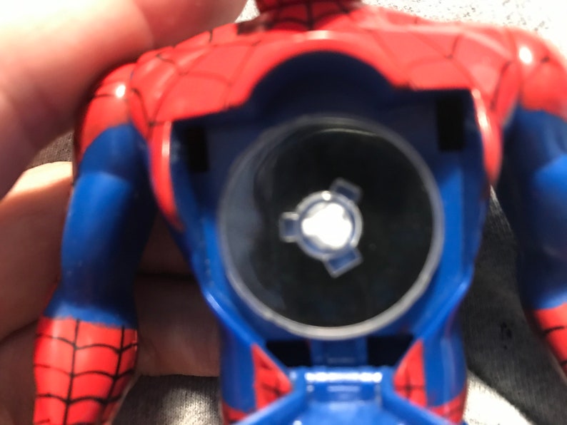 May include: A blue and red plastic action figure of Spiderman with a clear plastic disc on the back. The disc has a silver gear-like design in the center.