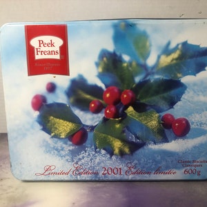 May include: A blue and white tin with a red holly sprig and red berries. The tin has the text "Peek Freans" and "Since/Depuis 1857" on the front. The text "Limited Edition 2001 Edition limitee" and "Classic Biscuits Classiques 600g" is on the bottom of the tin.
