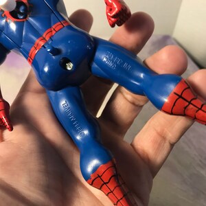 May include: A red and blue plastic action figure of Spider-Man. The figure has a web design on the suit and is holding its hands up in a rock and roll pose. The figure is made by Toy Biz Inc. and is copyright 1997 Marvel.