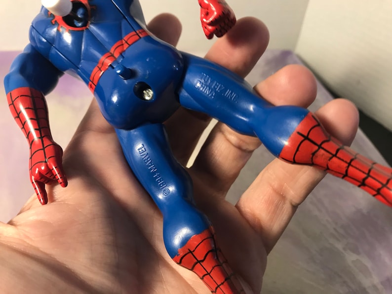 May include: A red and blue plastic action figure of Spider-Man. The figure has a web design on the suit and is holding its hands up in a rock and roll pose. The figure is made by Toy Biz Inc. and is copyright 1997 Marvel.