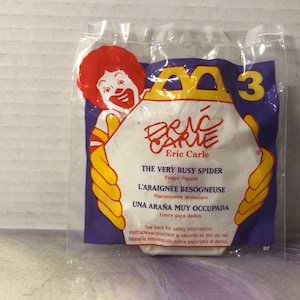 May include: A white plastic bag with a McDonald's Happy Meal toy inside. The toy is a finger puppet of a spider from the Eric Carle book "The Very Busy Spider". The bag has the title of the book and the number 3 on it.