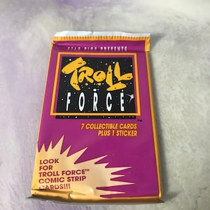May include: A purple and gold package of Troll Force trading cards. The package features the text "Troll Force" in a stylized font and the words "7 collectible cards plus 1 sticker". The package also includes the text "Look for Troll Force™ comic strip cards!!!".