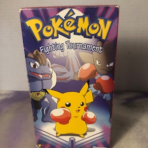 May include: A VHS tape case featuring the Pokemon logo and the text "Fighting Tournament". The case has a blue background with a red border and features images of Pikachu, Hitmontop, and Poliwhirl wearing boxing gloves.