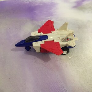 May include: A white, red, and blue toy airplane with wheels. The airplane has a cockpit and wings.