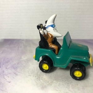 May include: A green toy jeep with a moon character wearing sunglasses and a brown jacket driving the jeep.