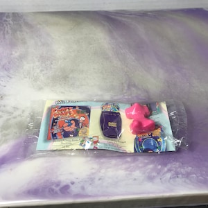 May include: A plastic bag containing a set of three Crazy Bones toys. The toys are a purple bag, a pink figure, and a blue and green game board. The bag has the words "Crazy Bones" printed on it. The game board has the words "Crazy Bones" and "Go Go Go! Crazy Bones!" printed on it.