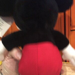 Puede incluir: Un juguete de peluche Mickey Mouse negro y rojo. El juguete est&aacute; de pie sobre una superficie amarilla.
